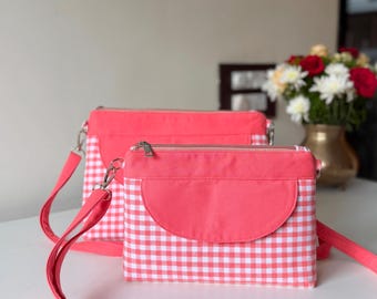 May include: Two rectangular crossbody bags featuring a vibrant coral pink solid fabric top panel and a white and coral pink gingham checkered pattern on the lower section. Each bag includes a matching coral pink flap and a silver zipper closure.