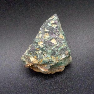 May include: A green and brown rock with white and purple flecks. The rock has an irregular shape and a rough texture.