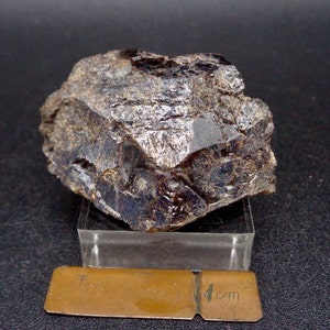 May include: A dark brown, rough, and angular mineral specimen with a crystalline structure. The mineral is approximately 4 cm in size and is displayed on a clear glass platform.