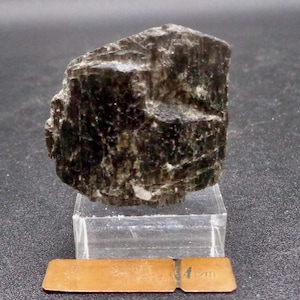 May include: A dark gray, rough-textured, irregularly shaped mineral specimen. The mineral is about 2 inches in size and is sitting on a clear acrylic stand.