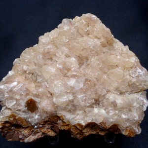 Op de afbeelding: Een cluster van doorschijnende, lichtroze kristallen op een bruine rotsbasis. De kristallen zijn in een ruwe, natuurlijke formatie geclusterd.