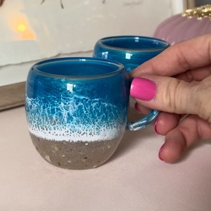 May include: Two ceramic mugs with a blue, white, and brown ocean wave design. The mugs have a handle and are perfect for coffee or tea.
