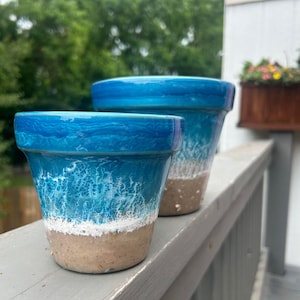 Puede incluir: Dos macetas de cerámica azul y blanca con un diseño de olas. La maceta más pequeña está delante de la más grande.