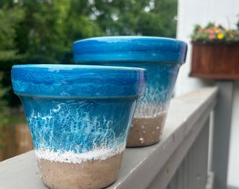 Può includere: Due vasi in ceramica blu e bianca con un design a onde. Il vaso più piccolo è davanti a quello più grande.