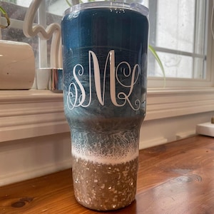May include: A blue and white ombre tumbler with a gold glitter bottom. The tumbler has a clear lid and a white monogram "SMK" on the side.