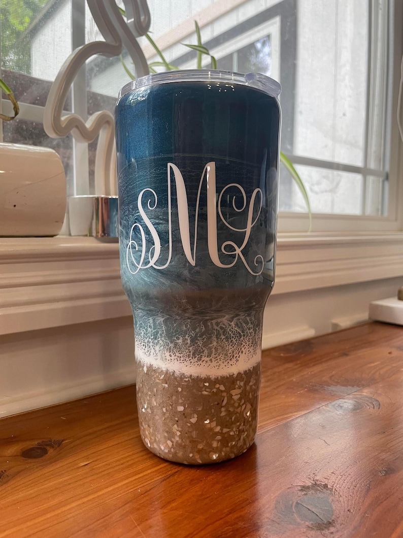 May include: A blue and white ombre tumbler with a gold glitter bottom. The tumbler has a clear lid and a white monogram "SMK" on the side.