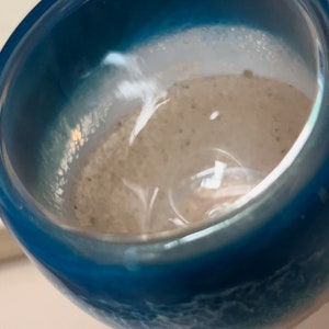 May include: A close-up of a blue and white resin cup with a textured surface. The cup is filled with a light brown liquid.
