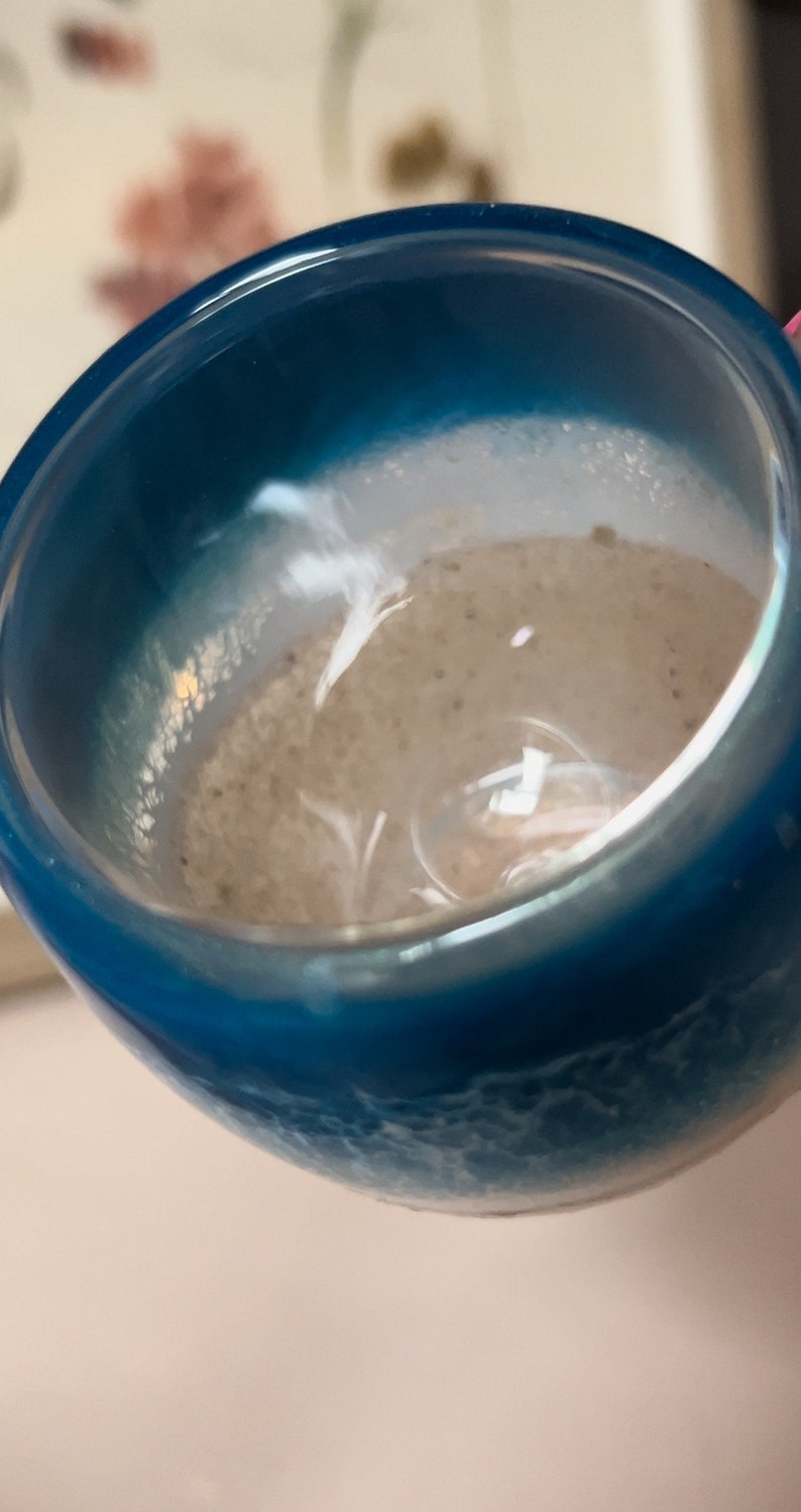 May include: A close-up of a blue and white resin cup with a textured surface. The cup is filled with a light brown liquid.