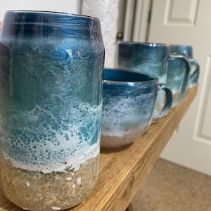 Peut inclure: Ensemble de quatre tasses &agrave; caf&eacute; sur le th&egrave;me de l'oc&eacute;an avec un sch&eacute;ma de couleurs bleu, blanc et marron. Les tasses sont d&eacute;cor&eacute;es d'un motif de vagues et d'un fond sablonneux.