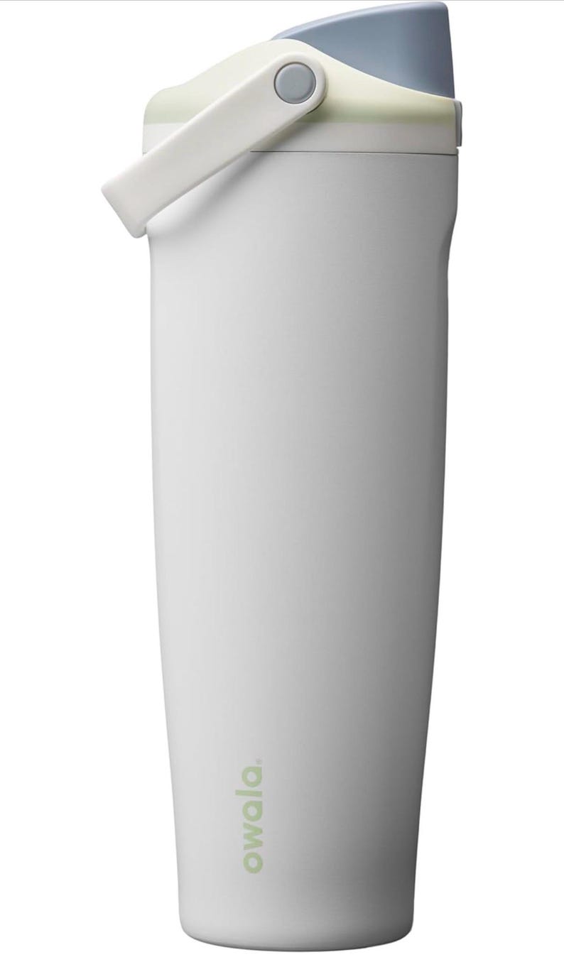 May include: White insulated water bottle with a light blue lid and a white handle. The bottle has the word "owala" printed in a light green color on the side. The handle is attached to the lid with a gray button.
