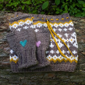 May include: Brown knitted fingerless gloves with a white and yellow geometric pattern and colorful heart accents. The gloves are on a tree trunk.