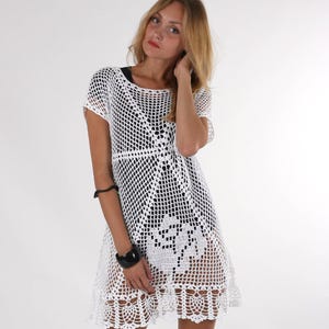 May include: White crochet dress with a short sleeve and a scalloped hem. The dress is made of a lightweight, airy fabric and is perfect for summer.