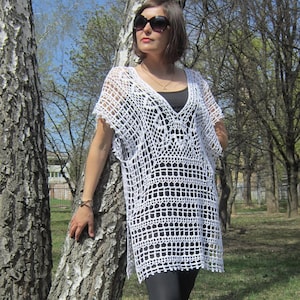 May include: White crochet tunic top with a V-neckline and short sleeves. The top is made of a delicate, open-weave fabric and has a flowing, relaxed fit.