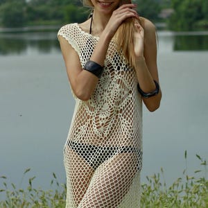 May include: A white crochet beach cover-up with a delicate floral pattern. The cover-up is sheer and has a loose fit.