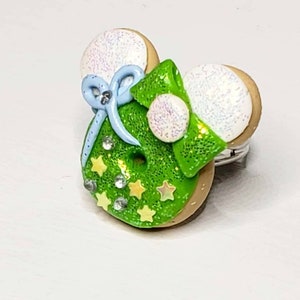 May include: A green and white ring with a bow and stars. The ring is made of polymer clay and is shaped like a donut.