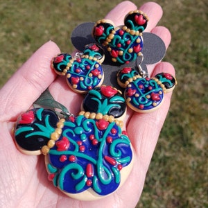 May include: Three pairs of Mickey Mouse-shaped earrings featuring intricate floral designs in shades of blue, green, red, and gold. The earrings are crafted from polymer clay and have a whimsical, fairytale-inspired aesthetic.