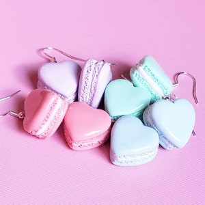 Könnte beinhalten: Ohrringe in Form von Herzen und runden Makronen in Pastellfarben, darunter Rosa, Lavendel, Mint und Blau. Die Ohrringe haben silberne Haken und sind auf einer rosa Oberfläche angeordnet.
