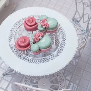 May include: Three pairs of polymer clay earrings, two are pink and one is green. The earrings are shaped like roses and a Mickey Mouse head. The earrings are on a white table with a white chair.