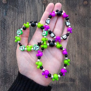 May include: Three colorful bracelets with black, green, and purple beads. The beads feature skull, ghost, and Mickey Mouse designs.