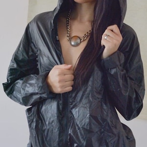 Könnte beinhalten: Eine Frau trägt eine schwarze Kapuzenjacke mit einer silbernen Kettenkette. Die Jacke ist offen und die Frau schaut nach rechts.