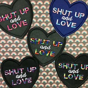 May include: Five black heart-shaped patches with rainbow embroidery. Each patch says "Shut Up and Love" in white lettering.
