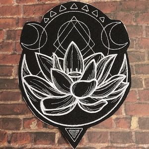 Pode incluir: Etiqueta bordada preta com um desenho de flor de lótus branca, cercada por um padrão geométrico e luas crescentes.