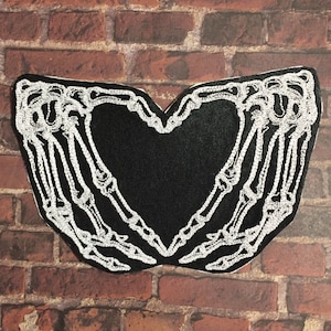May include: Black fabric patch with a white embroidered design of two skeleton hands forming a heart shape.