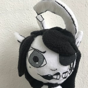 May include: Black and white plush toy with a single eye, an eyepatch, and a toothy grin. The toy has a black and white striped tail and a black and white striped horn.
