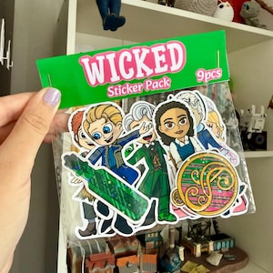 May include: A clear plastic bag containing a 9-piece sticker pack labeled WICKED. The stickers feature cartoon-style characters in green and blue outfits, a green potion bottle with a holographic finish, and a circular gold emblem with pink stripes.