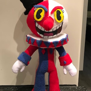 May include: A handmade plush toy of a jester with a red and blue costume, a white face with black eyes and a red nose, and a black top hat.