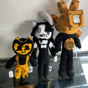 May include: Three plush toys from the video game Bendy and the Ink Machine. The toys are a black and white character with a bow tie, a yellow and black character with a large head, and a yellow and black character with a large head and a camera.
