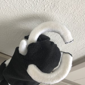May include: Black and white plush toy with a white loop on top. The toy is made of soft, fuzzy fabric.