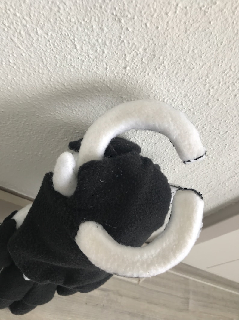 May include: Black and white plush toy with a white loop on top. The toy is made of soft, fuzzy fabric.