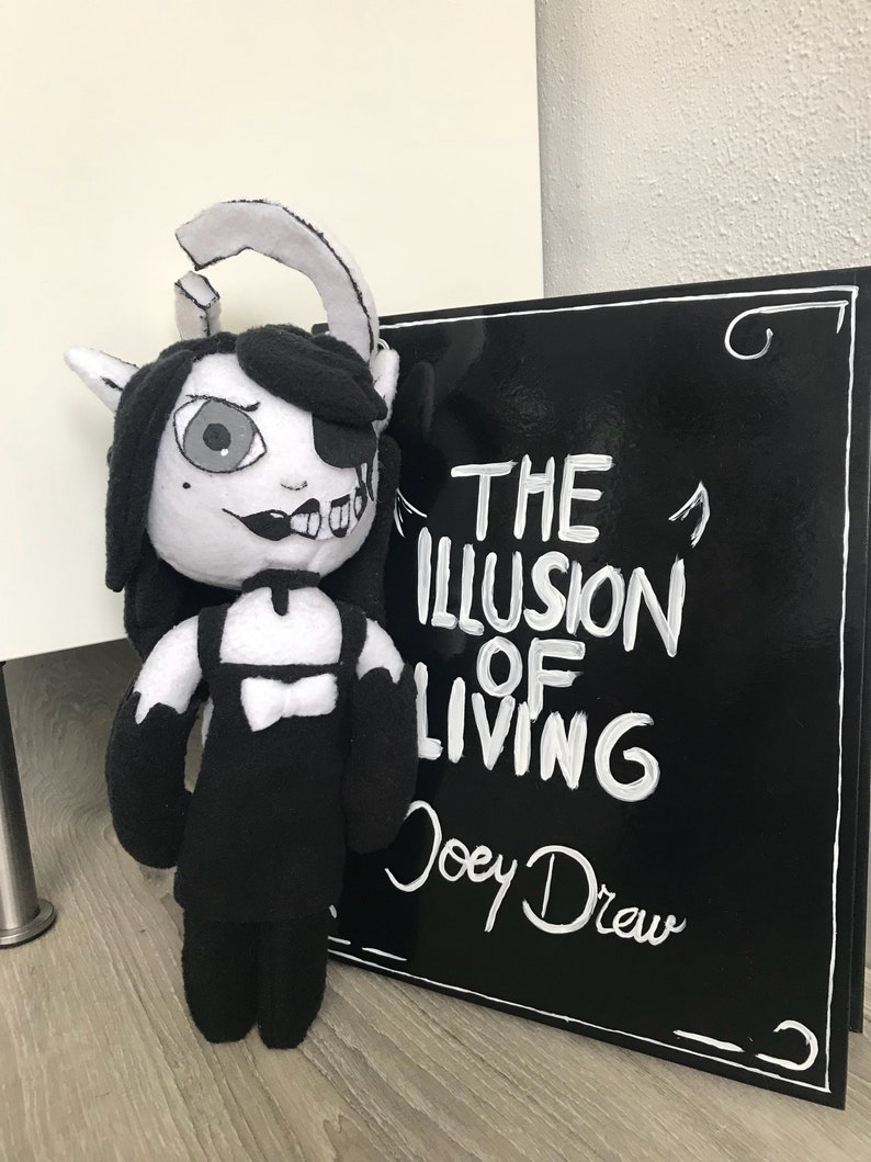 May include: Black and white plush toy of a character with a black dress and horns. The toy is standing next to a black sign with white text that reads "The Illusion of Living Joey Drew".