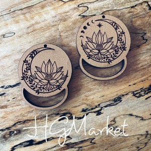 May include: Two wooden round ornaments with a crescent moon design and a lotus flower inside. The moon has a star and three crescent moons inside. The ornaments are on a wooden surface.