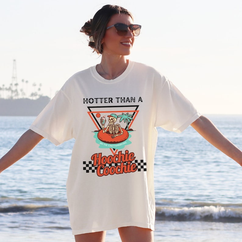 K&ouml;nnte beinhalten: Wei&szlig;es T-Shirt mit einem Grafikdruck eines Skeletts in einem Pool-Schwimmring mit dem Text "Hotter than a Hoochie Coochie" auf der Vorderseite.