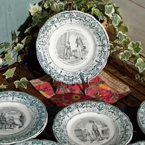 May include: Six vintage ceramic plates with green trim and black and white illustrations of people in various scenes. The plates are arranged in a circle on a wooden surface.