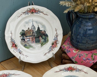May include: A set of ten white ceramic plates with a floral border and a painted scene of a village or countryside. The plates are stacked in two piles of five.