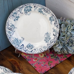 May include: Set of five white ceramic plates with a blue and white floral pattern. The plates are stacked on a wooden surface.