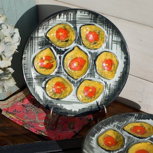 May include: Two black and white ceramic plates with a design of yellow and red circles in a circular pattern. The plates are on a wooden surface.