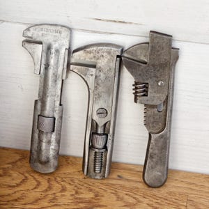 Puede incluir: Tres llaves inglesas vintage con mangos de metal. La llave inglesa de la izquierda tiene el texto "SIDARME" y "SUISSE" en el mango.