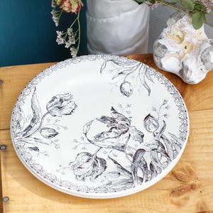 May include: A white ceramic plate with a black and white floral design featuring tulips and leaves. The plate has a decorative border.