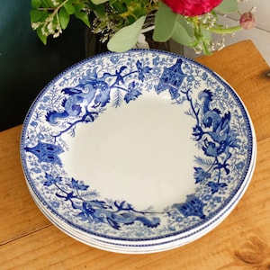May include: A stack of white ceramic plates with a blue floral and dragon design. The plates have a detailed border and are arranged on a wooden surface. The plates are part of a dinnerware set.