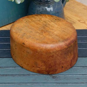 May include: A round wooden bowl with a natural brown finish. The bowl has a smooth, slightly textured surface and shows signs of age and use.
