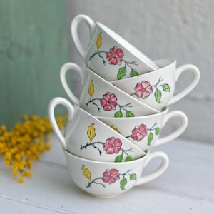 Peut inclure: Une pile de quatre tasses à thé blanches avec des motifs floraux. Les tasses présentent des fleurs roses, des feuilles vertes et des accents jaunes. Les tasses sont empilées en forme de pyramide.