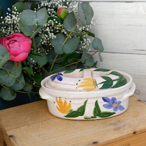 Peut inclure: Plat à four ovale en céramique blanche avec un couvercle. Le plat est décoré de feuilles vertes peintes à la main, de fleurs jaunes et bleues.