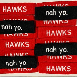 May include: A collection of red and black headbands. The red headbands have the word "HAWKS" embroidered in white. The black headbands have the phrase "nah yo." embroidered in white.