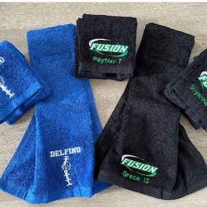 May include: An assortment of blue and black terrycloth towels. Some towels are folded, others are unfolded. The blue towels have the word "DELFINO" embroidered in white. The black towels have the word "FUSION" embroidered in green and white.