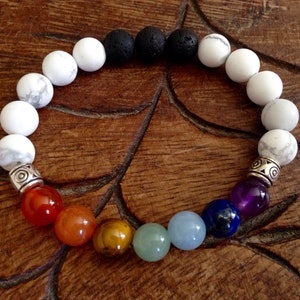 May include: A bracelet with white, black, and lava rock beads, followed by seven chakra stones in the colors of the rainbow: red, orange, yellow, green, blue, indigo, and violet.