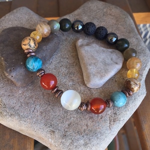 May include: A colorful beaded bracelet with copper accents. The beads are made of various stones, including lava rock, hematite, and moonstone.